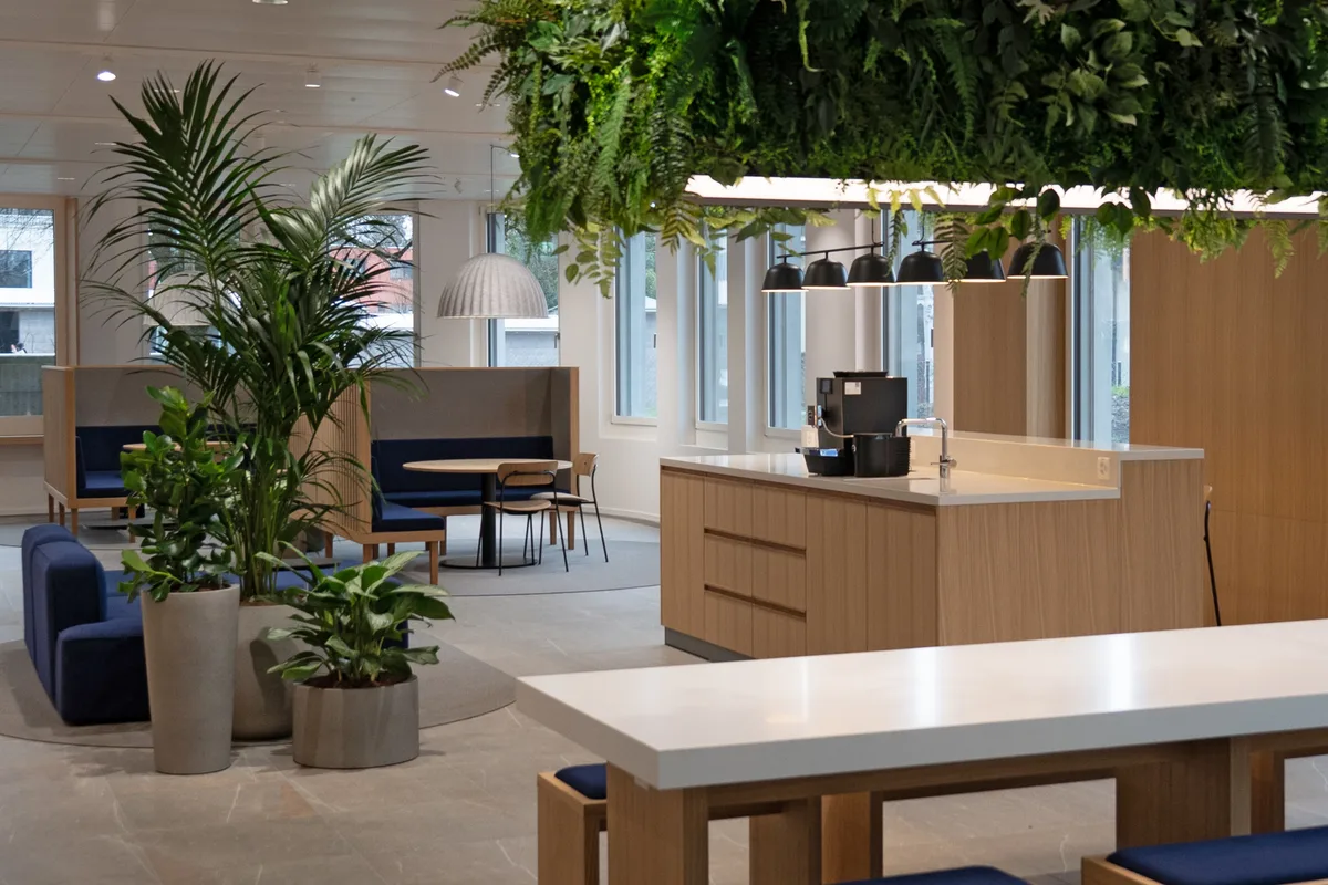 Offene Sitzecken und eine prominent platzierte Kaffeemaschine im Eingangsbereich im Erdgeschoss. Blick in den Empfangsbereich der ZKB-Filiale in Wetzikon. Sitzecken, Möbel aus hellem Holz und in der Mitte eine grosse Ablage mit einer Kaffeemaschine.